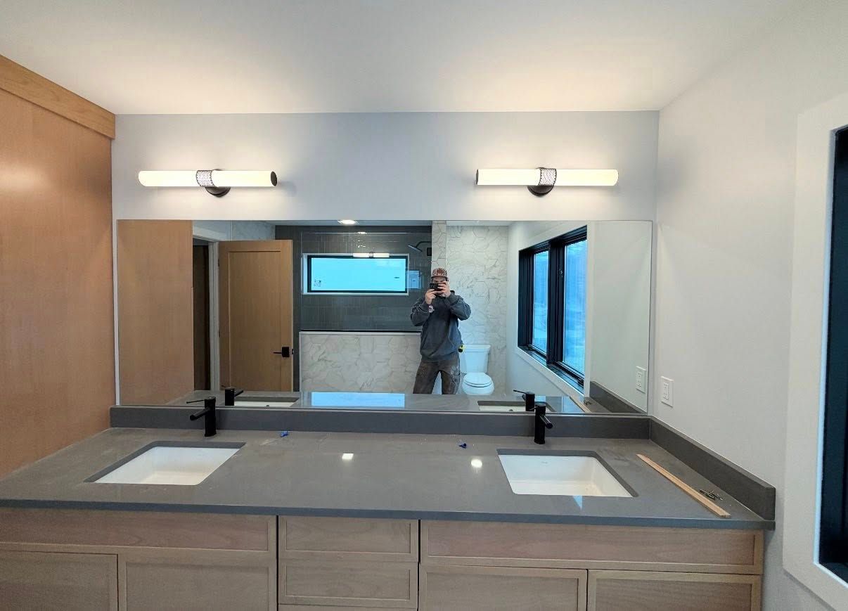 A modern double-sink bathroom vanity with wood cabinets, gray countertops, two mirrors, and overhead light fixtures.