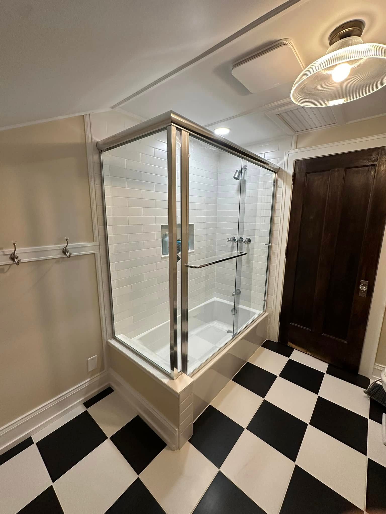 A bathroom corner with a bathtub featuring a glass enclosure, cream walls, and a black-and-white checkered floor.