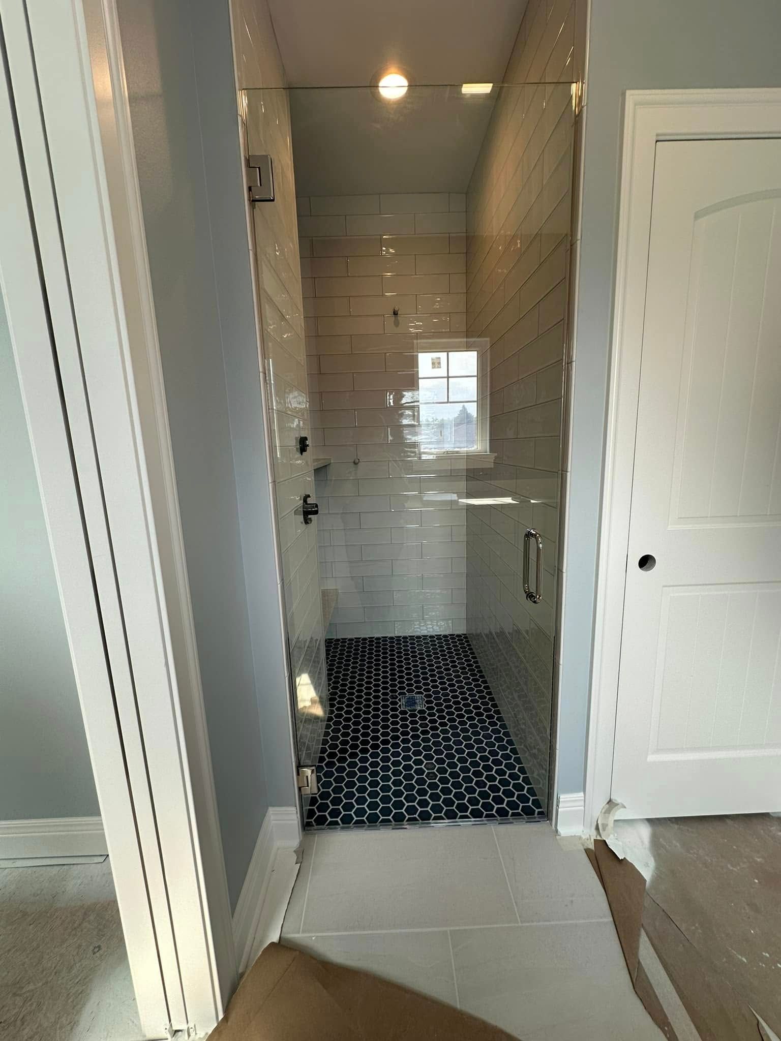 A bathroom shower area with white subway tile walls, a glass door, and a black and white patterned rug on the floor.