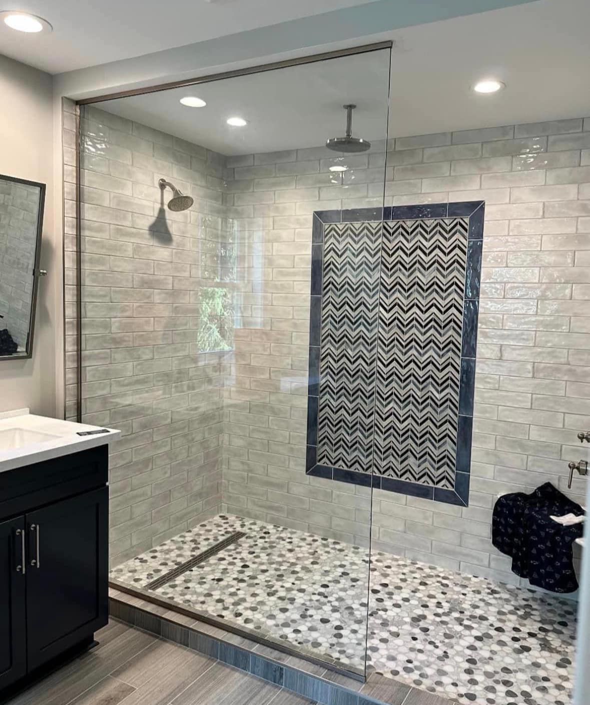 Modern walk-in shower with light brick walls, a patterned chevron accent, pebble floor, and a glass door.
