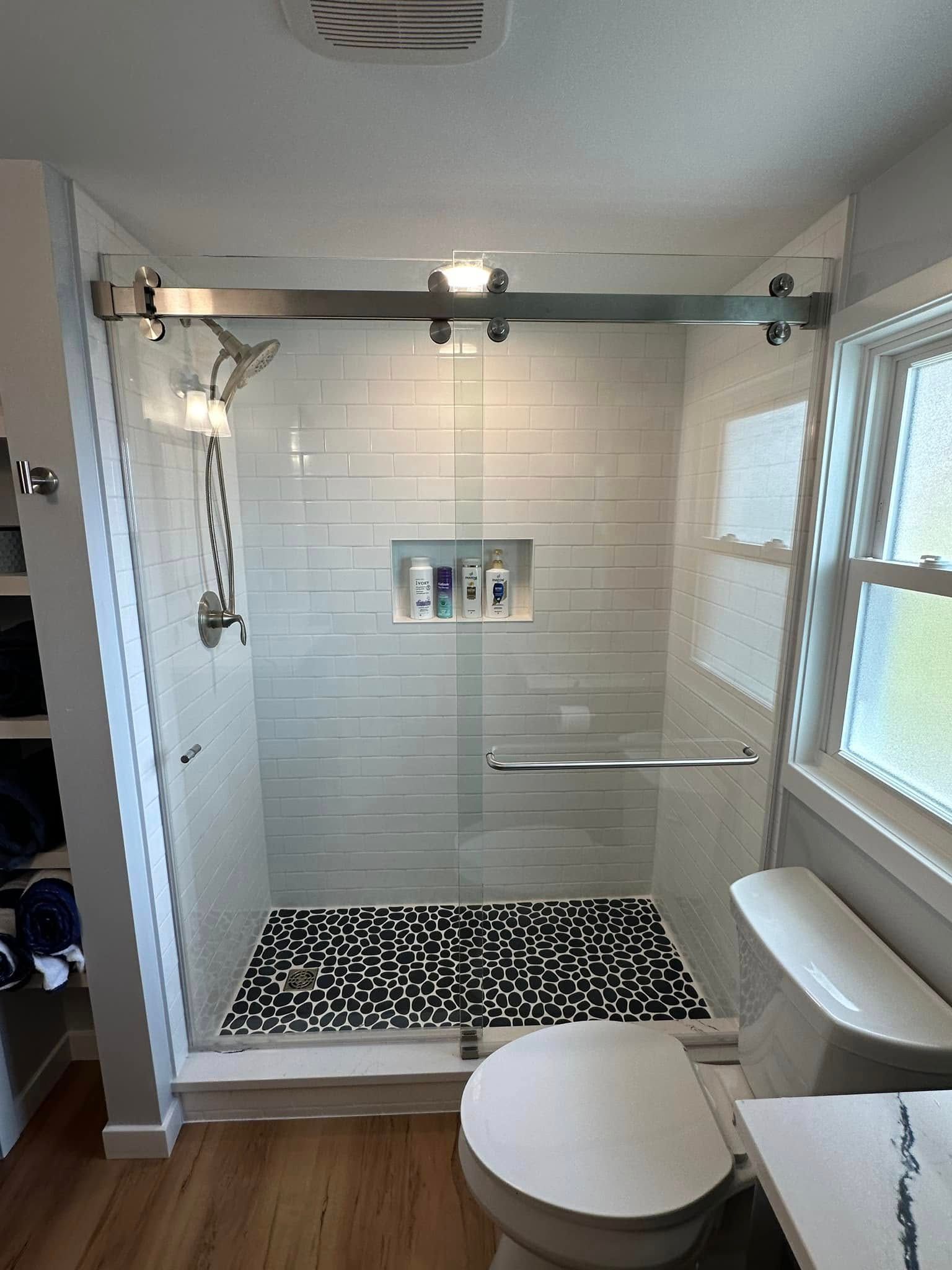 A modern bathroom with a glass-enclosed shower featuring white subway tile, a pebble floor, and a sliding door.