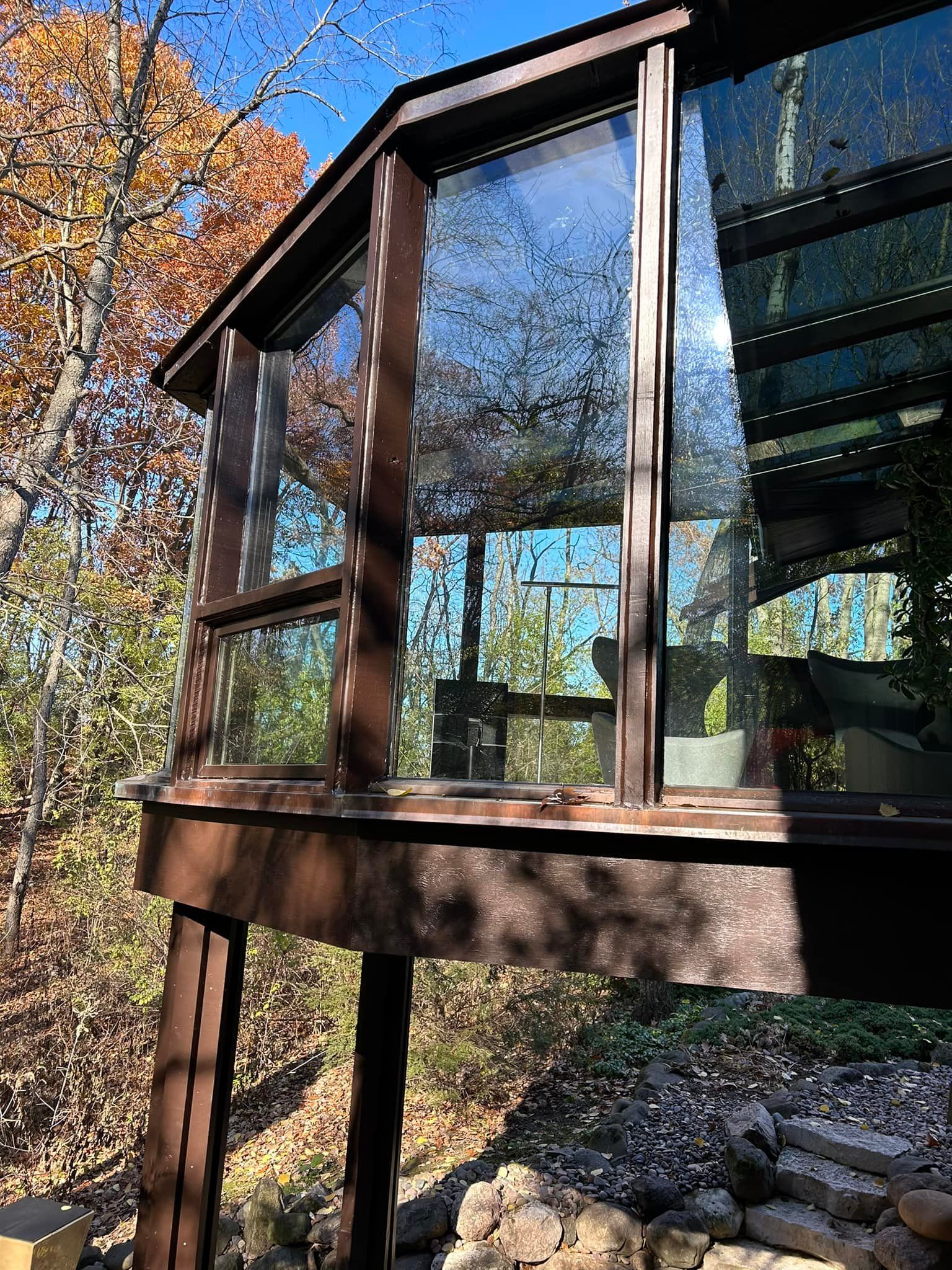 A raised wooden deck with large glass windows overlooking a wooded area with fall-colored trees.