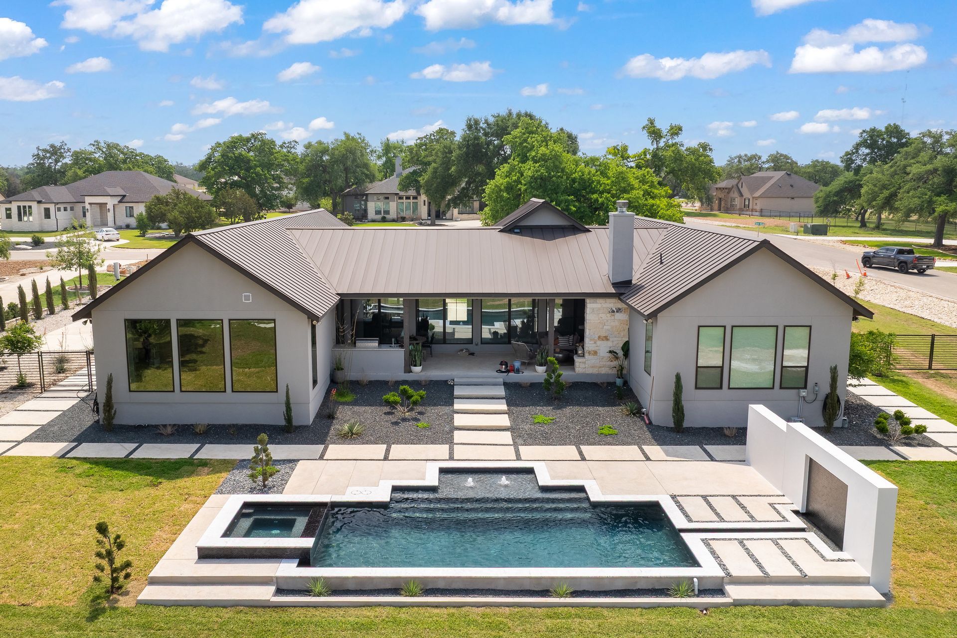 Modern gray house with pool and outdoor fireplace. Lush green lawn, blue sky.