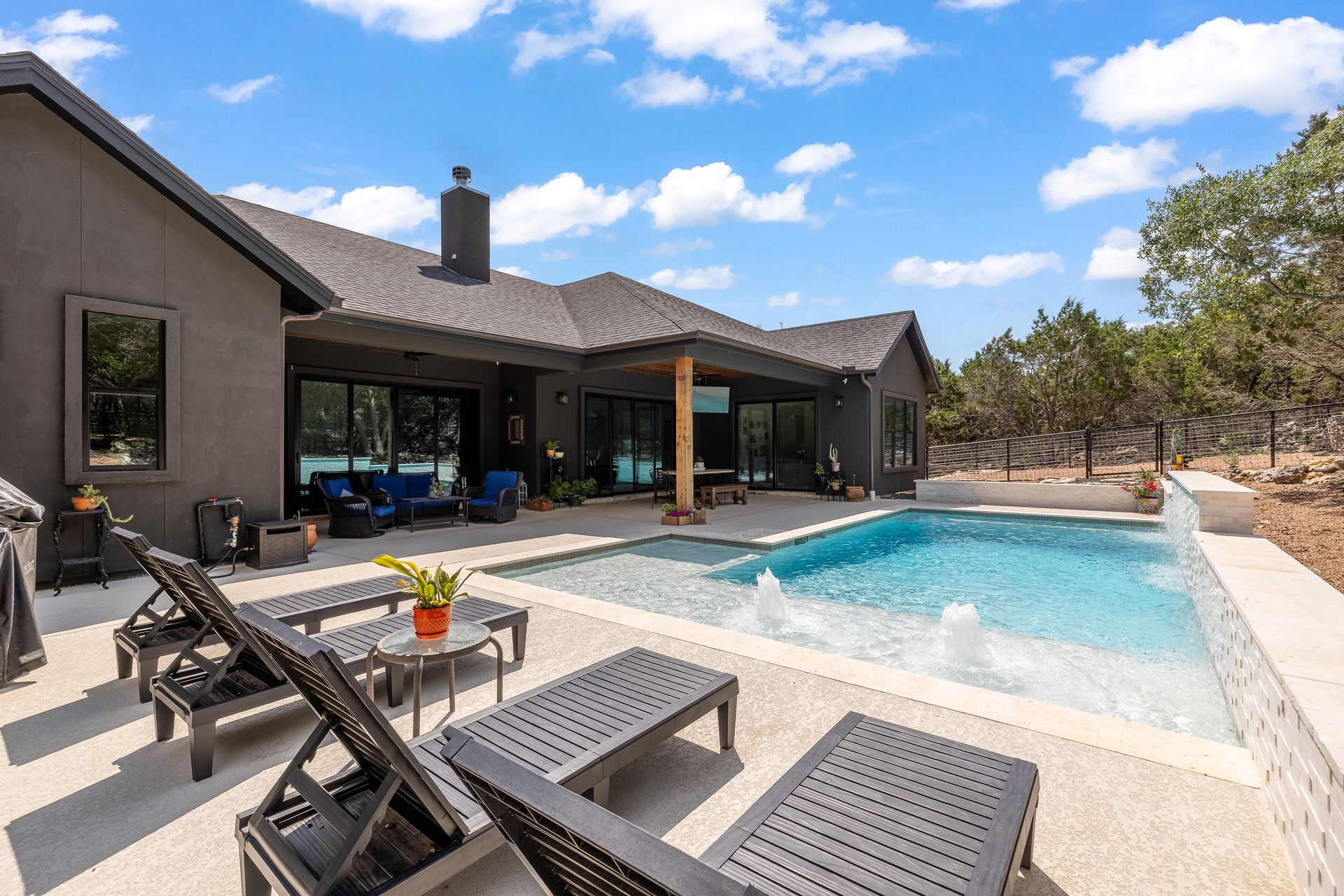 Backyard with pool and lounge chairs, dark gray house, blue sky.