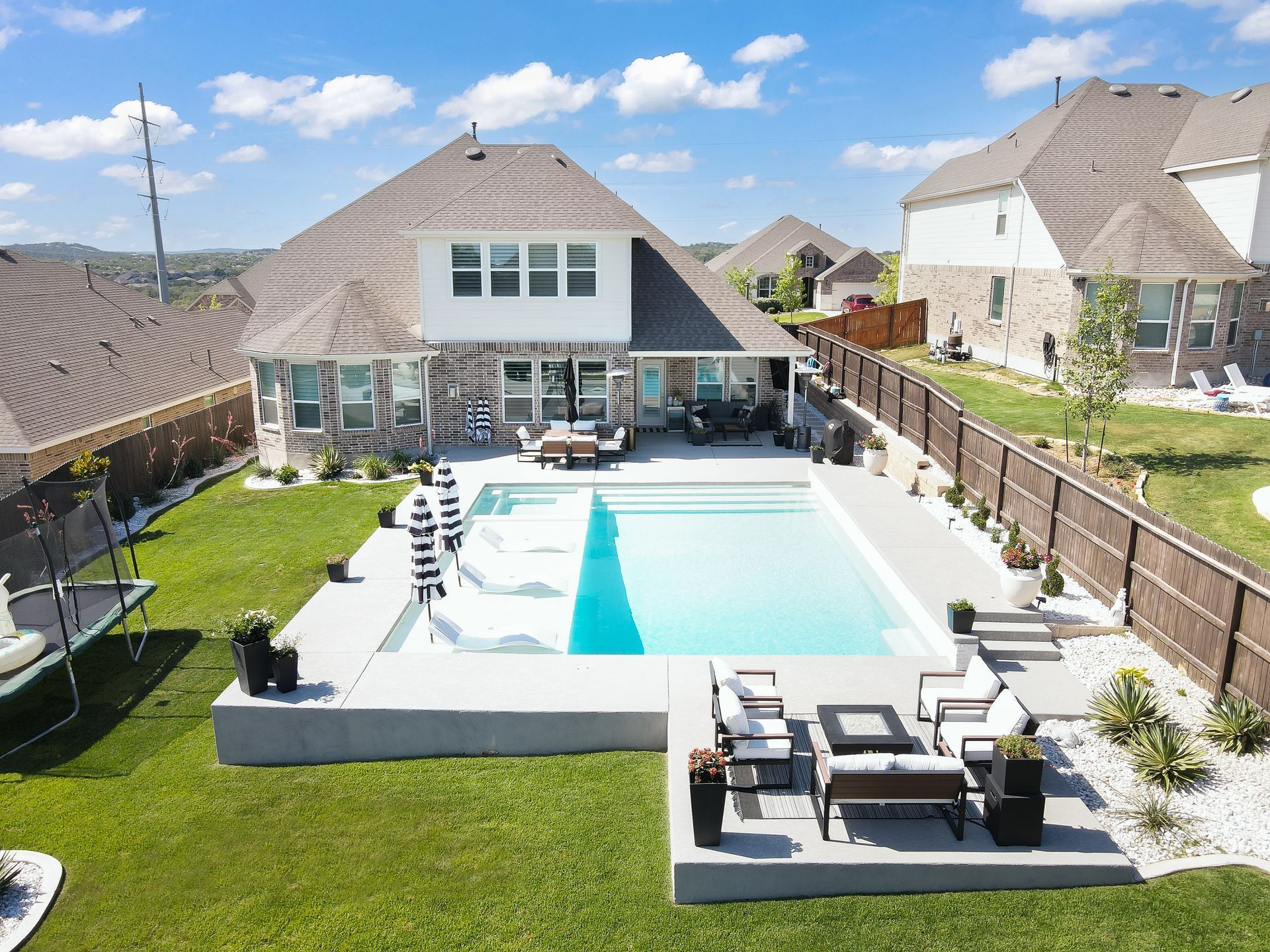 Backyard with pool and patio furniture in front of a two-story house under blue sky.