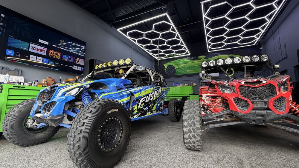 Blue and red off-road UTVs displayed in a showroom with a neon geometric ceiling