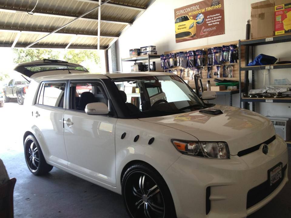 A white Scion xB parked inside a garage with its trunk open, featuring custom wheels and fender vents.