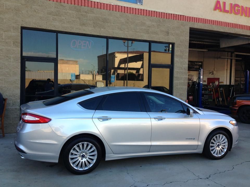 A silver Ford Fusion sedan parked in front of an automotive repair shop with glass windows and an 