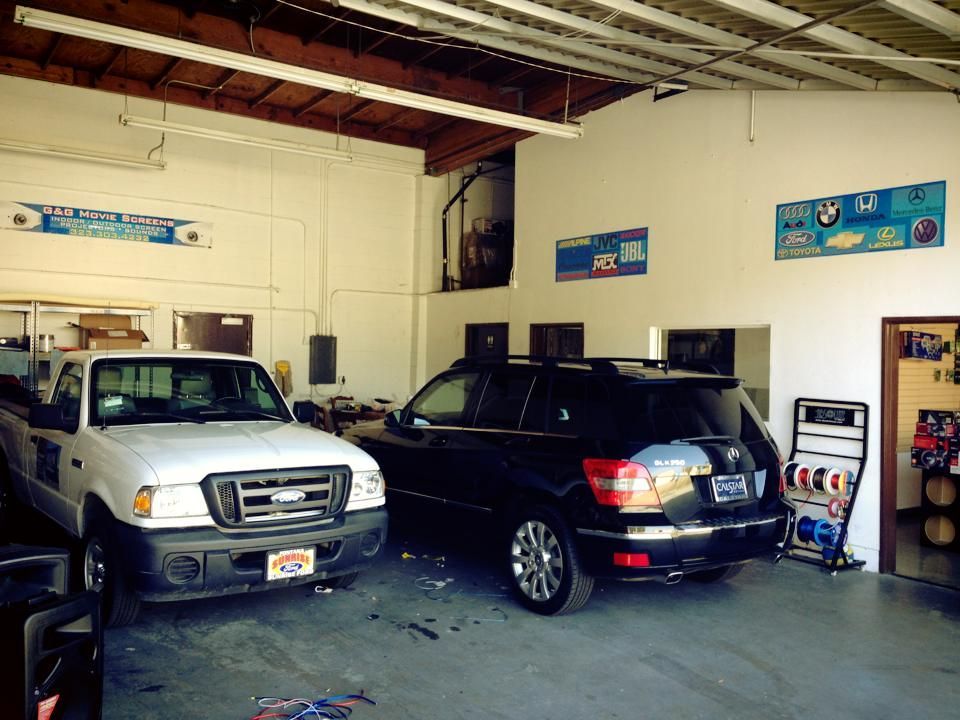 A white pickup truck and black SUV parked inside a vehicle repair garage with brand logos on the white walls.
