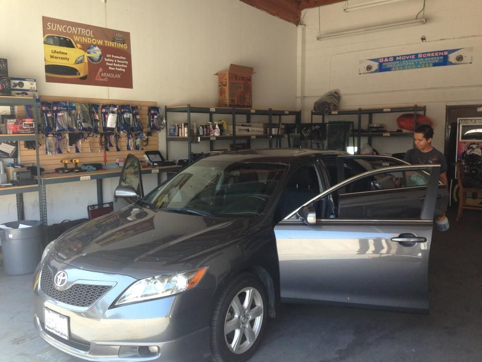 A dark grey sedan with its doors open parked inside an automotive workshop with shelves of equipment and car parts.