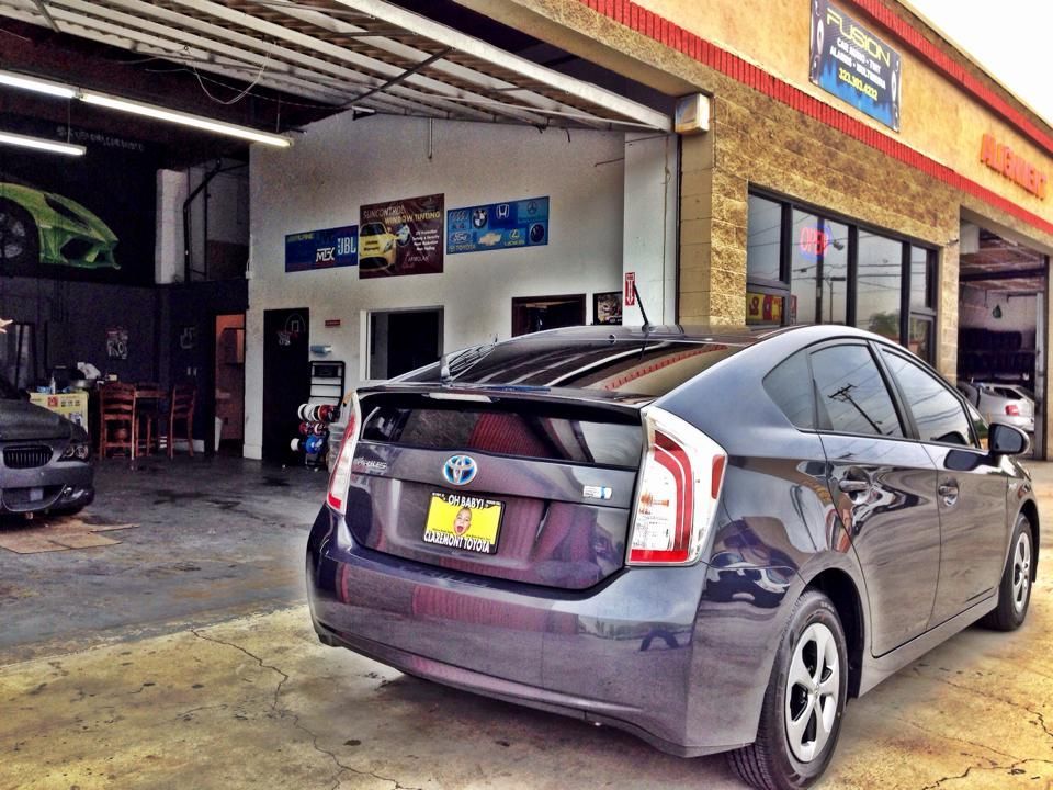 A gray Toyota Prius parked in front of an automotive repair shop under an open garage bay.