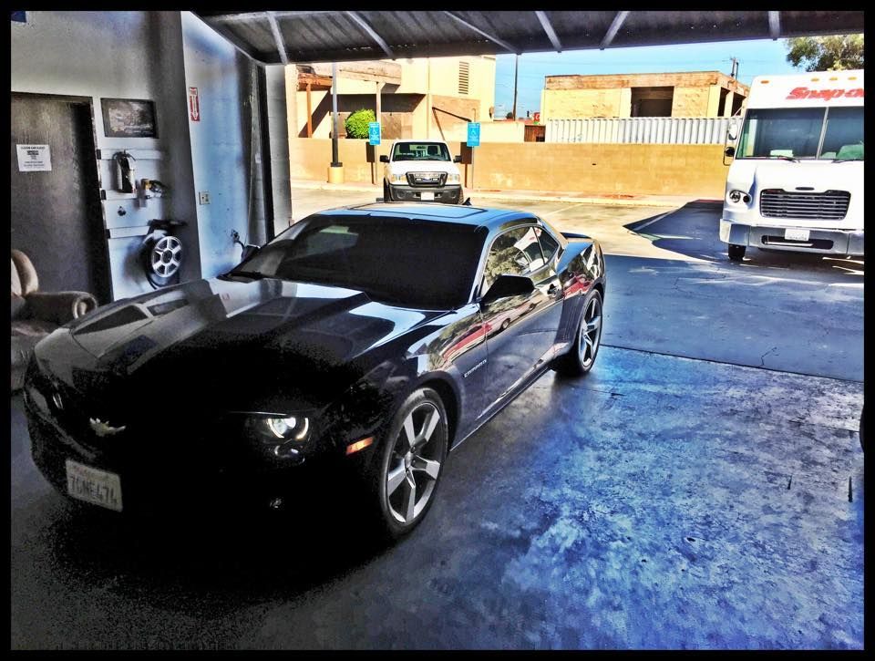 A shiny black Chevrolet Camaro parked in a garage with a white delivery truck visible in the background.