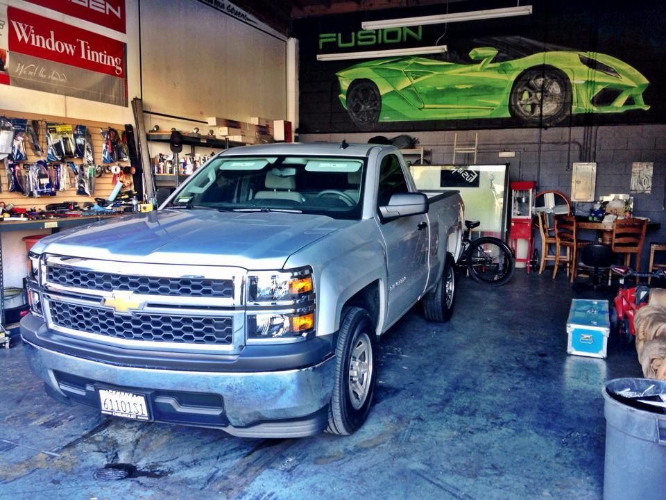 A silver Chevrolet pickup truck parked inside a repair shop, with a green sports car mural on the back wall.