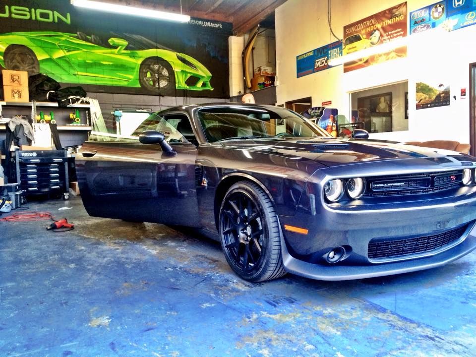 A dark gray Dodge Challenger parked inside an auto shop with a large green car poster on the wall.