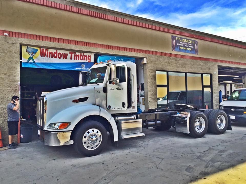 A large white semi-truck parked in front of an automotive shop with a window tinting banner.