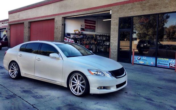 A white sedan with custom wheels parked in front of a commercial automotive shop.