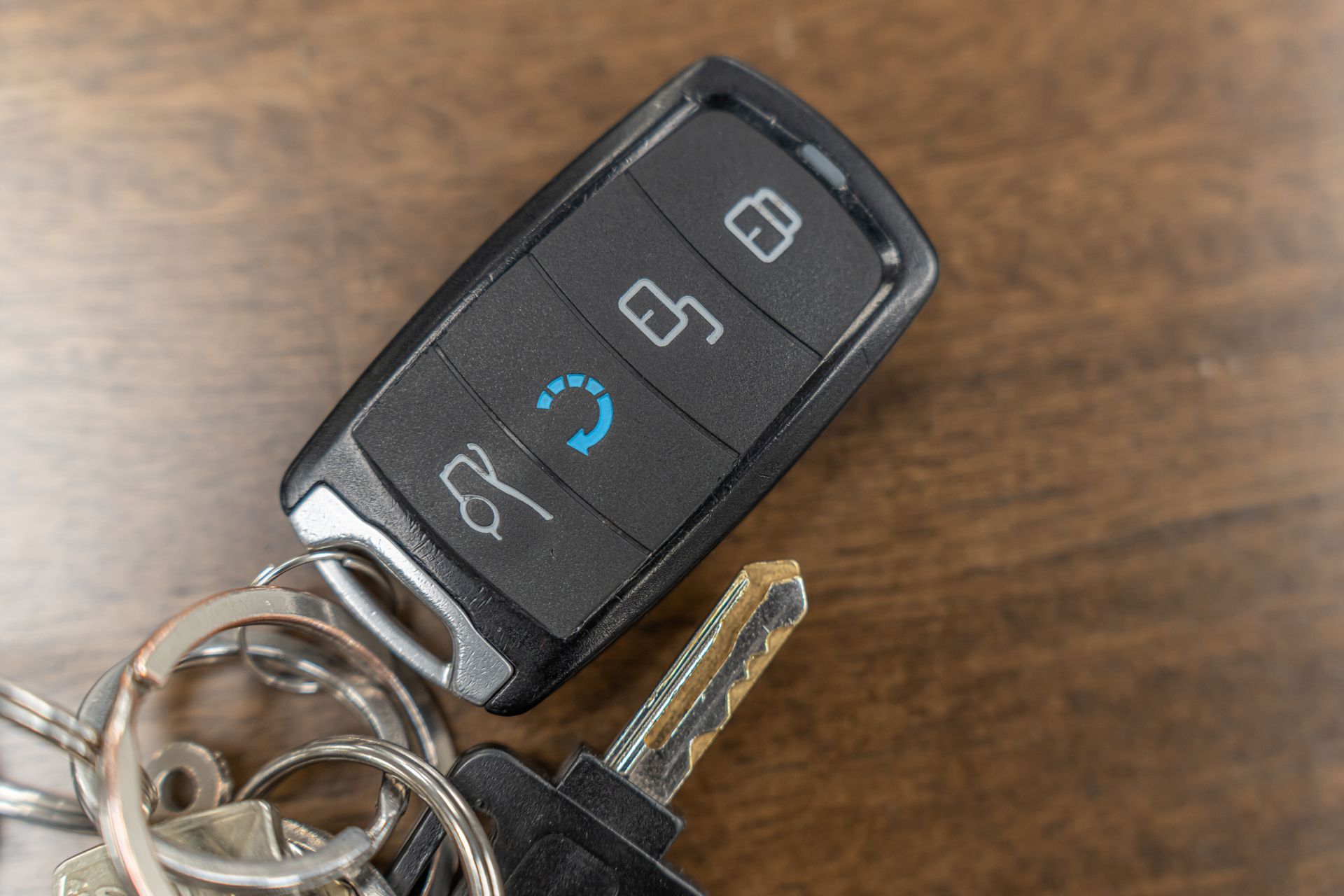 A car key fob with four buttons and a physical key attached to a ring, resting on a brown wooden surface.