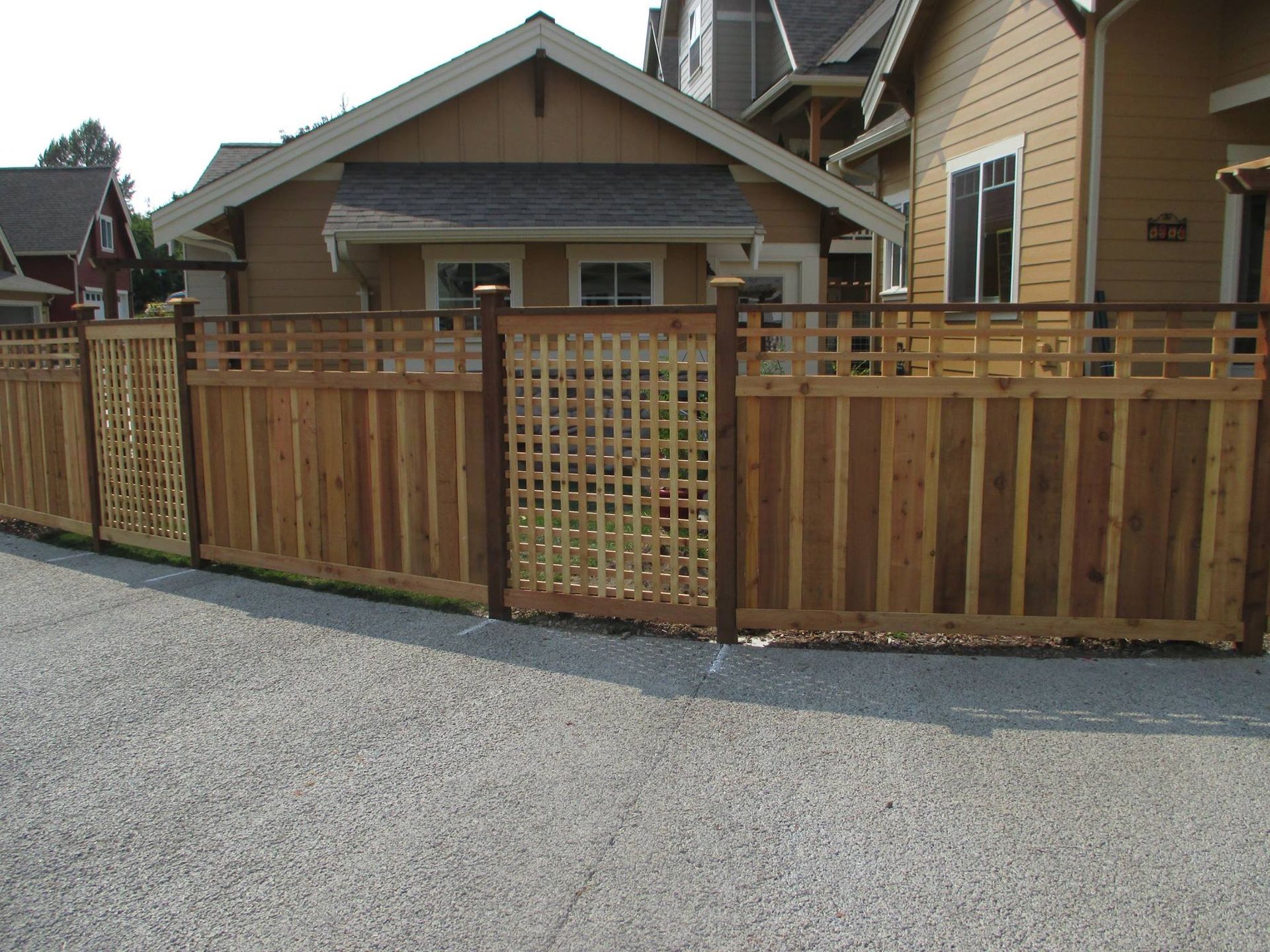 Wooden fence with lattice sections in front of tan houses.
