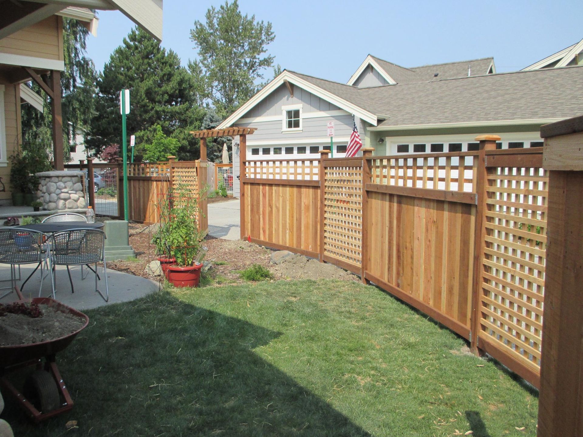 Wooden fence in a backyard, with a lawn, patio, and house in the background.