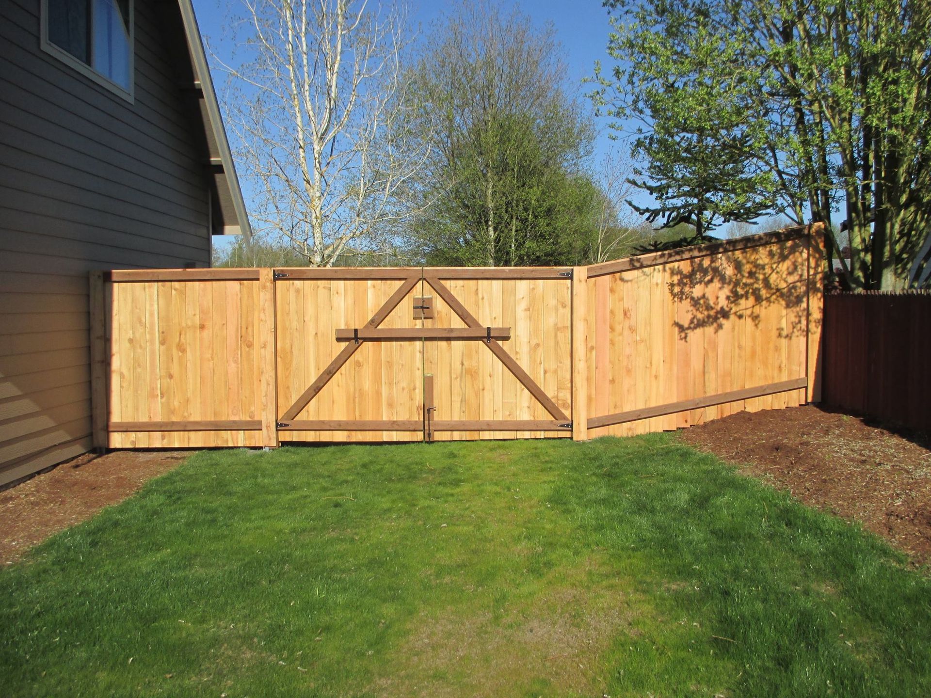 Wooden fence with gate in a grassy yard, adjacent to a house.