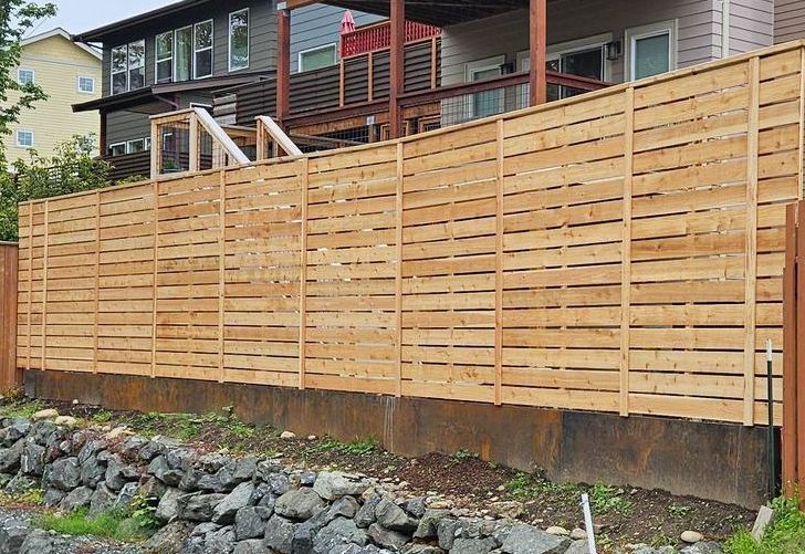 Wooden horizontal slat fence in front of a house, built on a rock wall foundation.