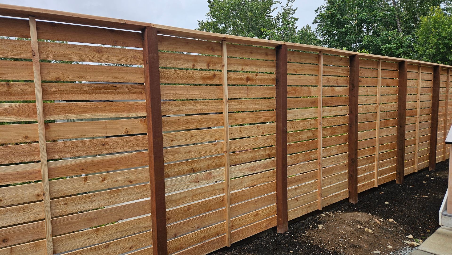 Wooden horizontal slat fence in a yard with dark brown posts and a light brown top rail.