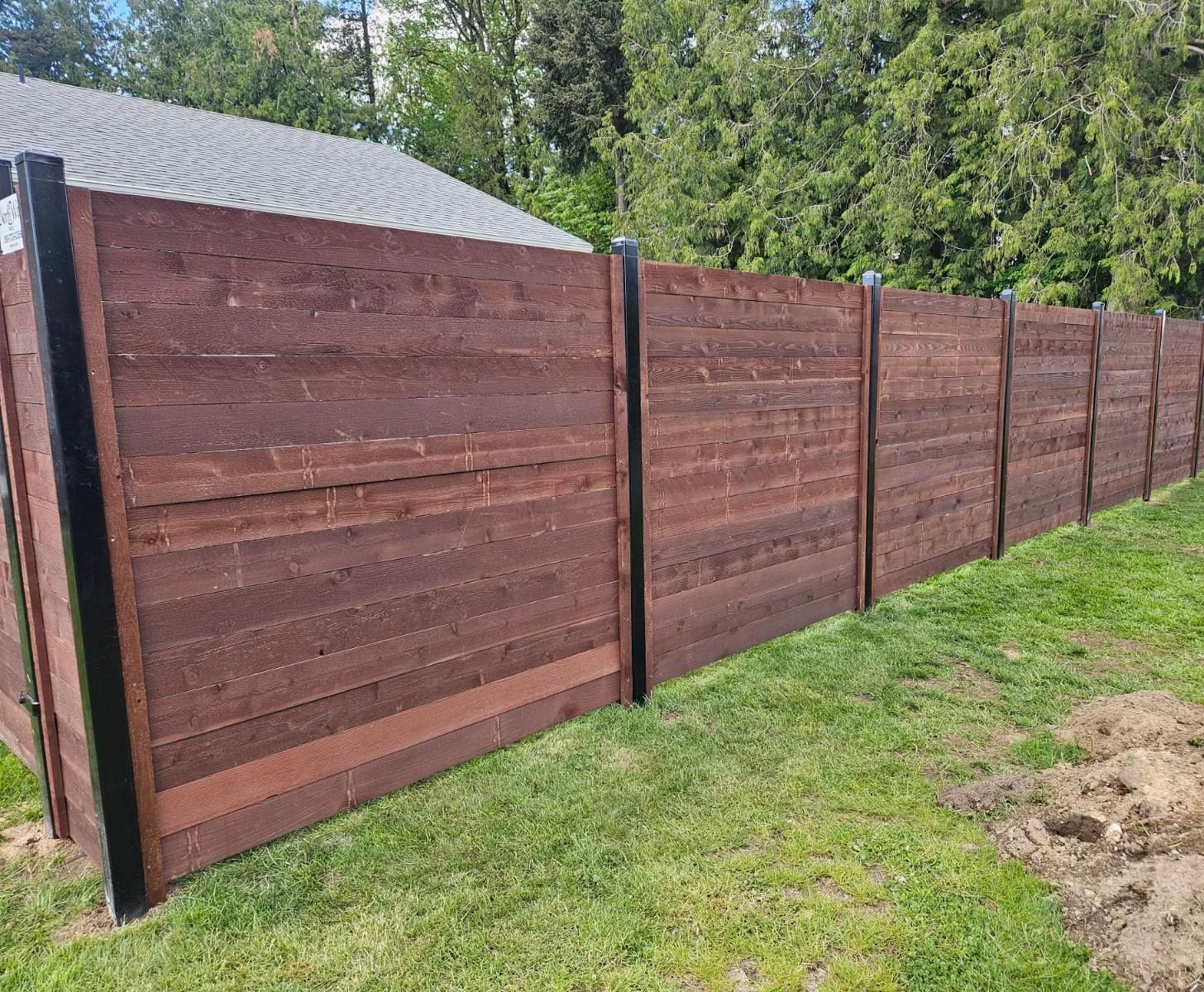 Brown wooden fence with black posts in a grassy yard, extending into the distance.