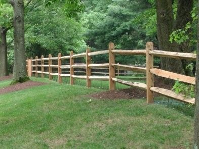 Wooden split-rail fence in a grassy yard, bordered by trees.