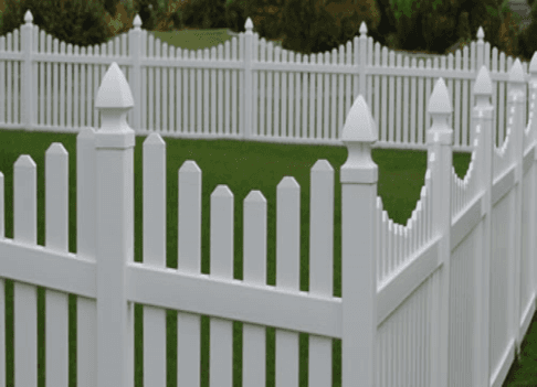 White picket fence, with decorative pointed caps, surrounds a green lawn.