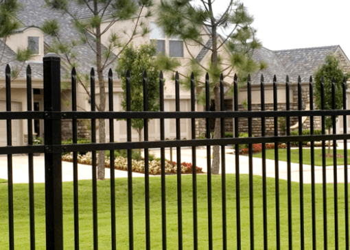 Black metal fence in front of a house with trees and a green lawn.