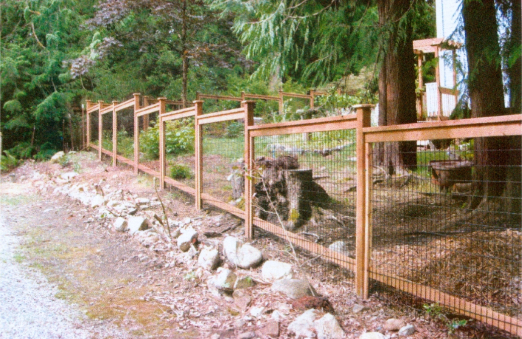 Wooden fence with wire mesh bordering a rocky area and trees.