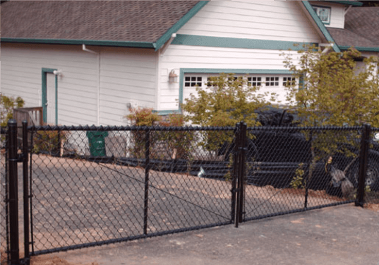 Black chain-link fence with a gate in front of a white house and garage, with green trim and trees.