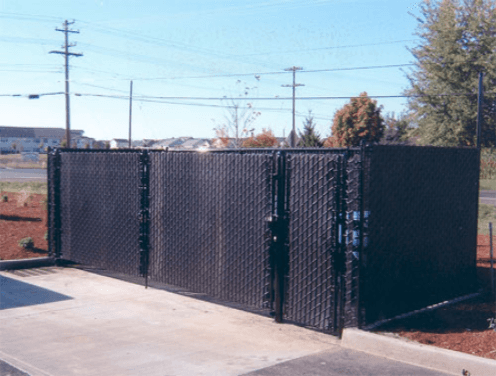 Black chain link fence with gates, enclosing a dumpster area, on a sunny day.