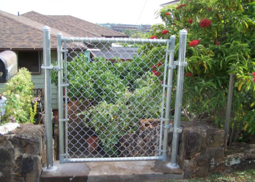 Chain-link gate in a yard, between stone columns. Green foliage visible behind the gate.