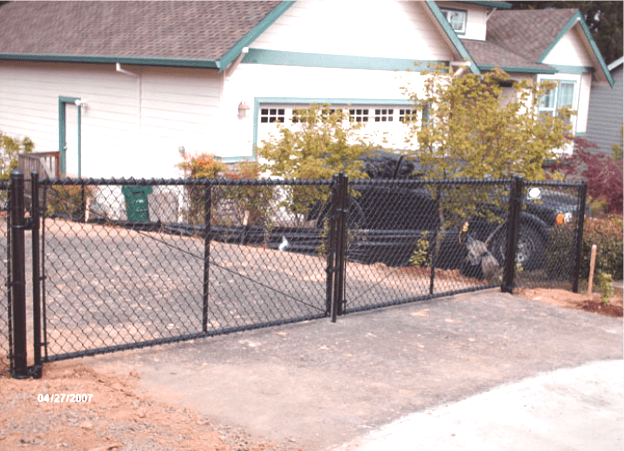 Black chain-link gate at the entrance of a driveway in front of a beige house.