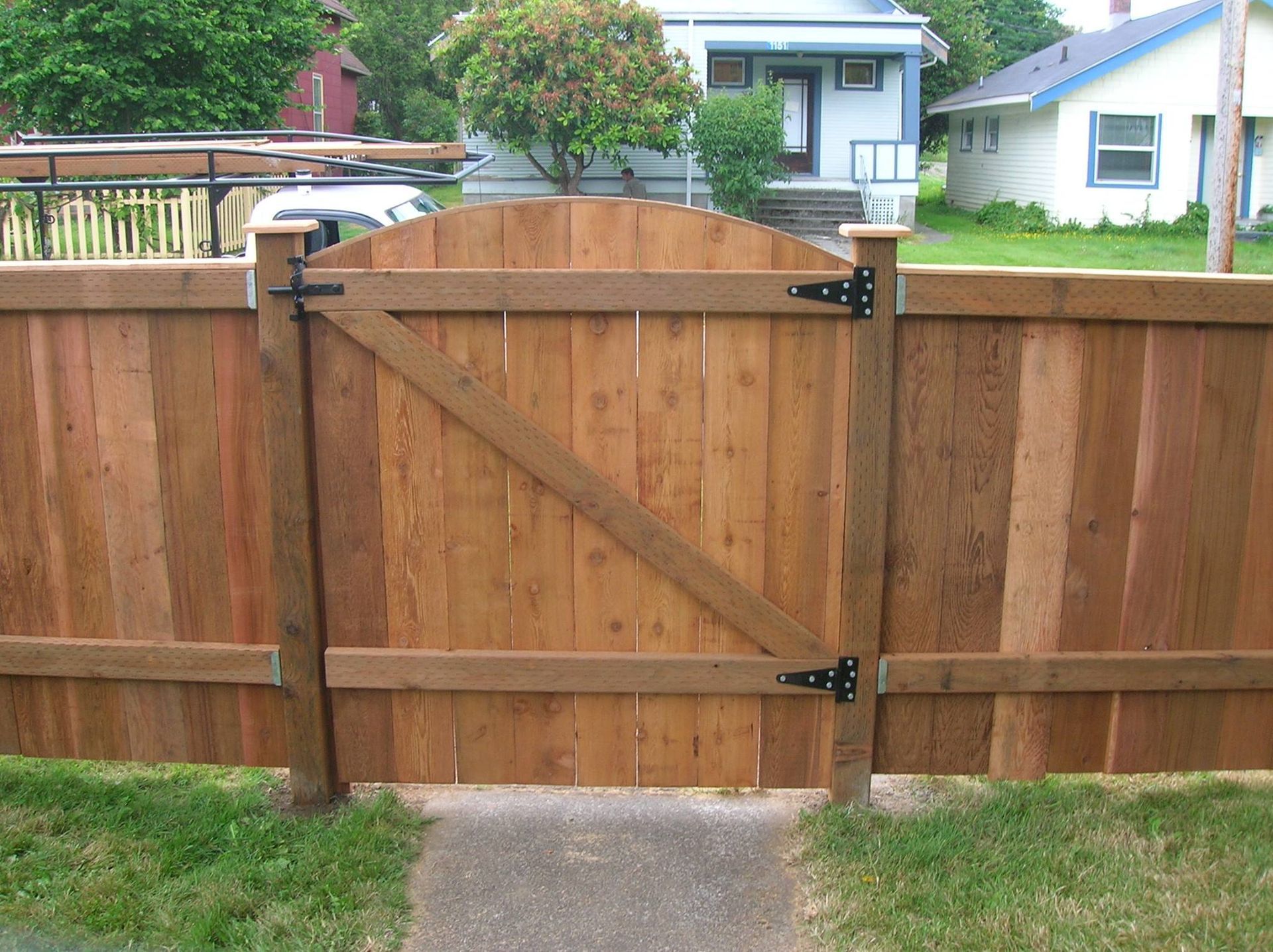 Wooden gate in a wooden fence. Brown wood. Black hinges. Green grass and path.