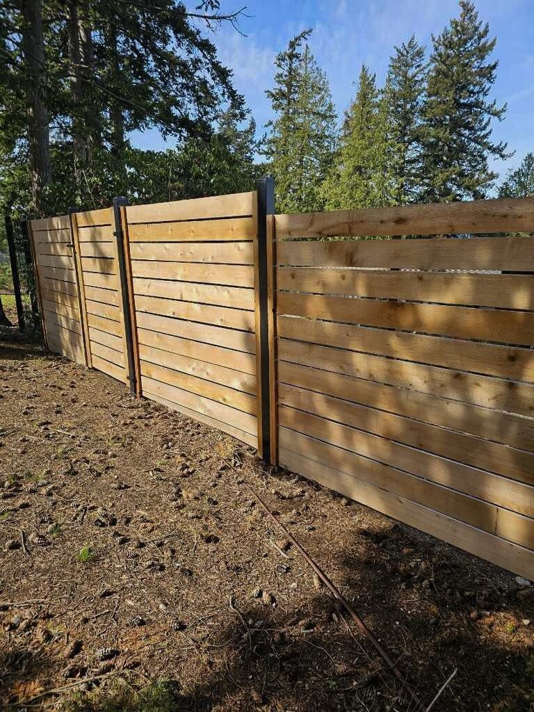 Wooden horizontal slat fence in a wooded area, on a sunny day.