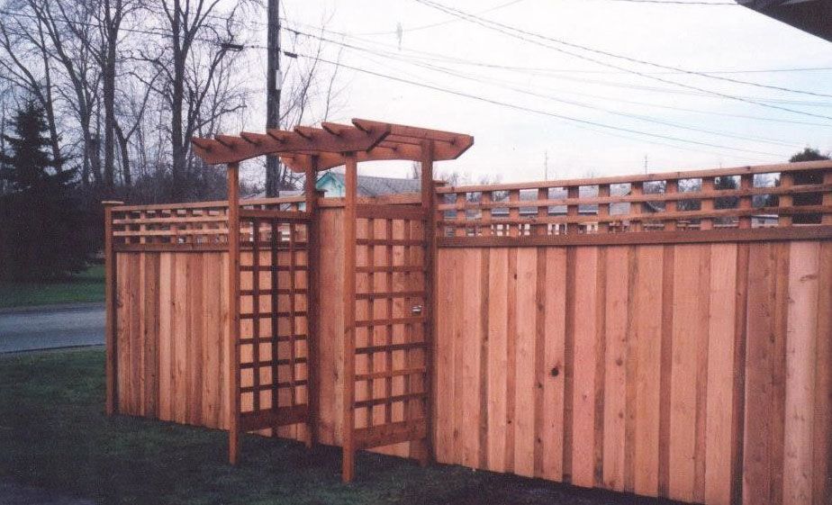Wooden fence with gate, trellis, and decorative top rail.