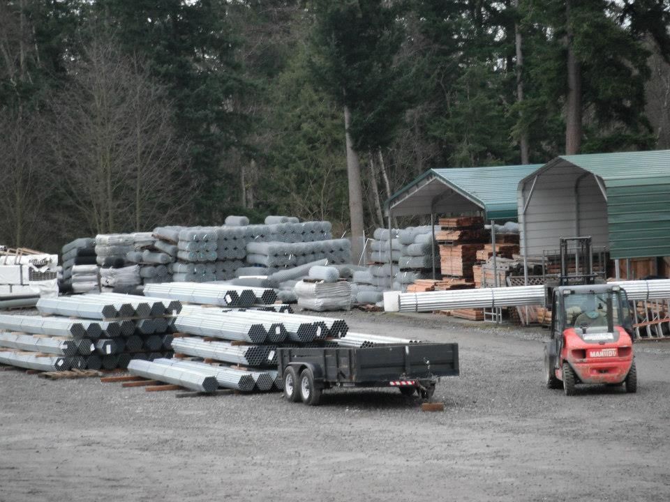 Forklift and trailer in a lumberyard with stacks of building materials.