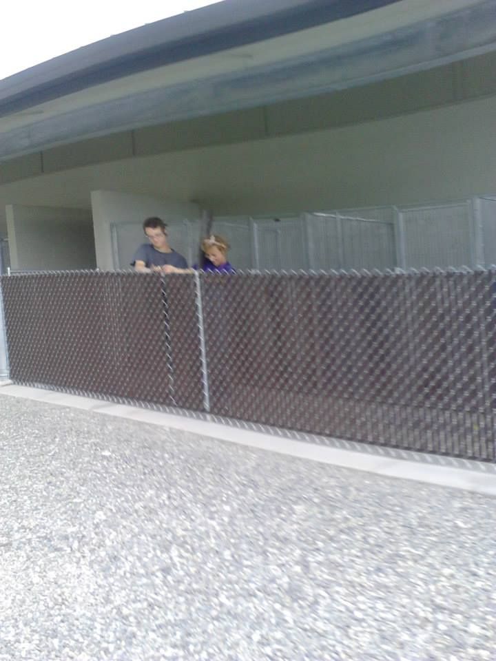 Two people leaning on a dark, textured fence, outdoors. Building overhang above.