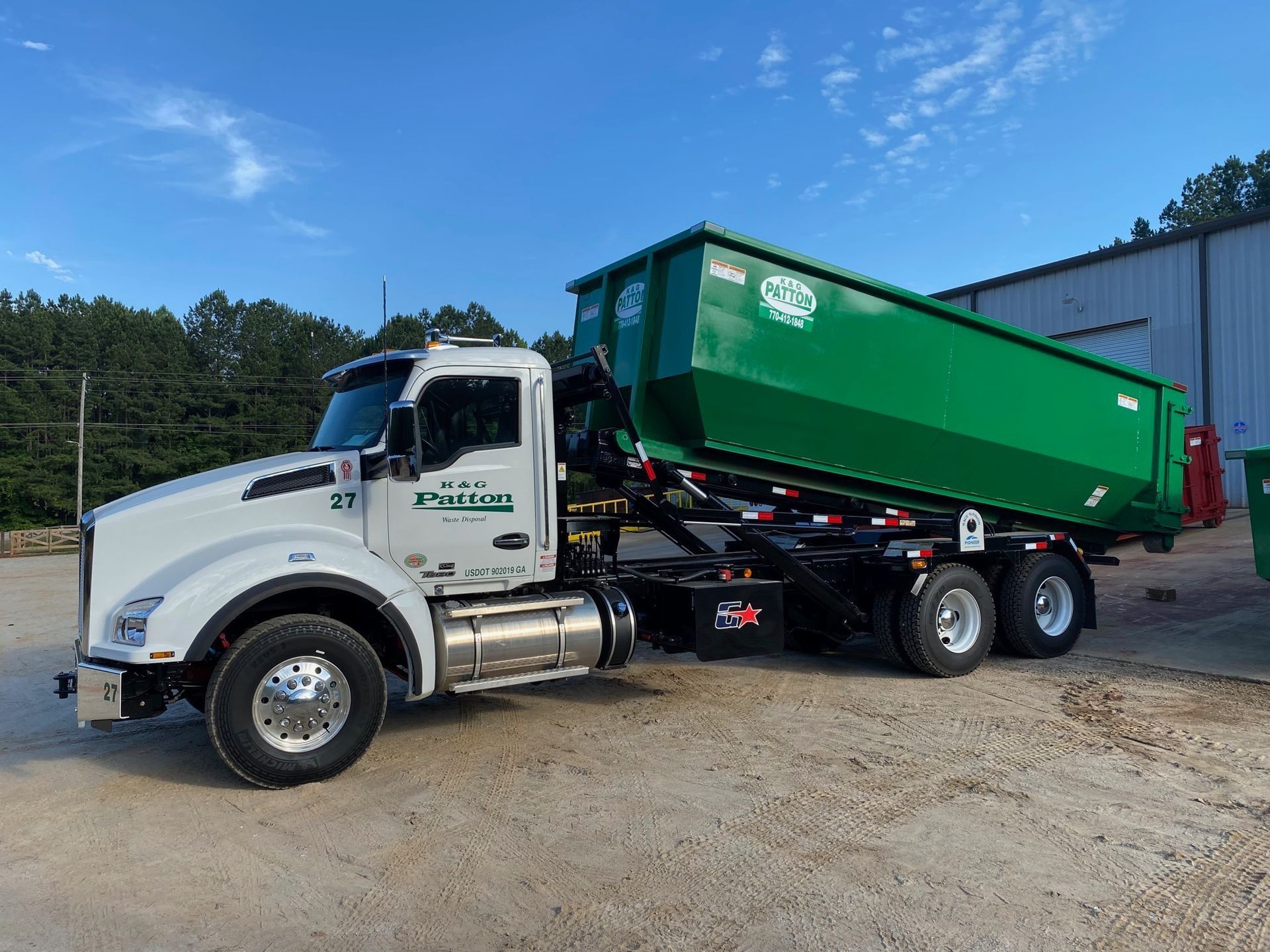 White and green dump truck with a green dumpster on a sunny day.