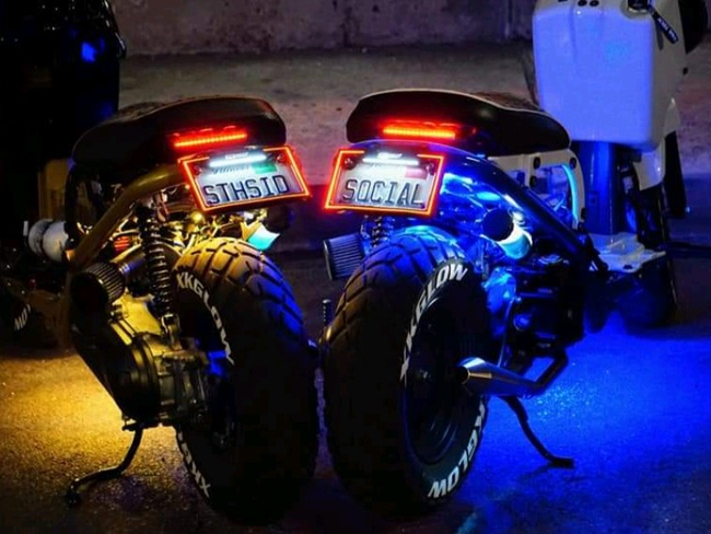 Two custom motorcycles parked at night with bright blue underglow and red tail lights