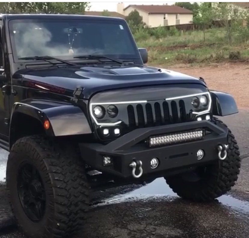 Black lifted Jeep Wrangler with off-road tires parked on a wet road near a grassy field.
