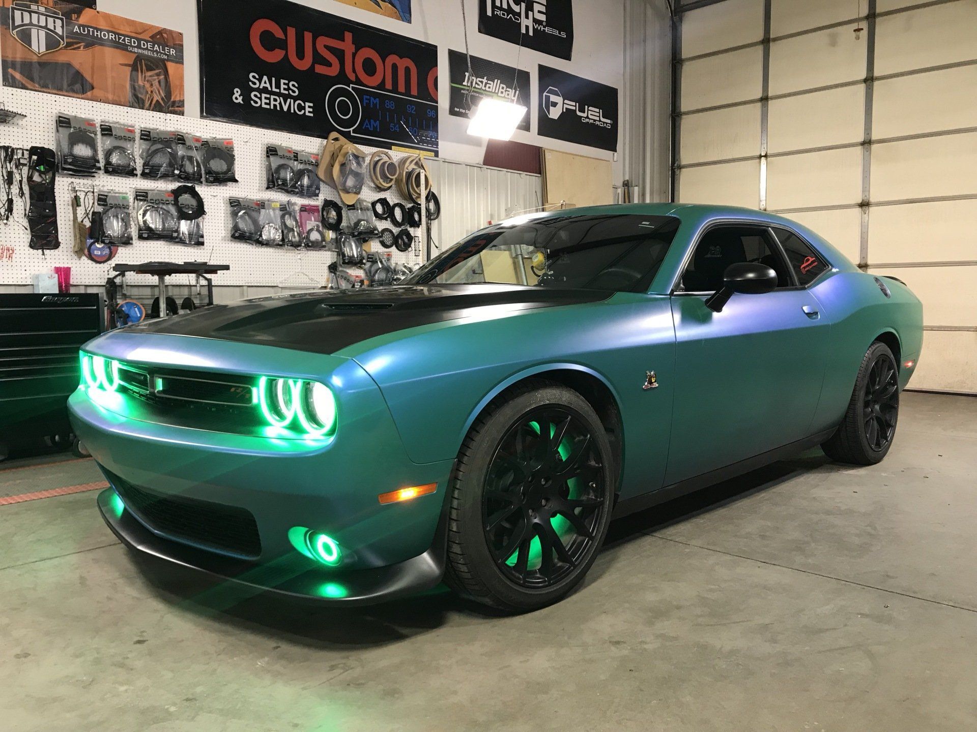 Green Dodge Challenger with neon green headlights parked in a garage showroom