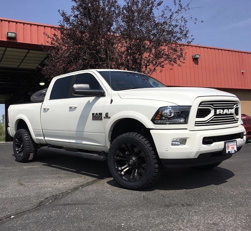 White RAM pickup truck with black wheels parked outside a red industrial building.