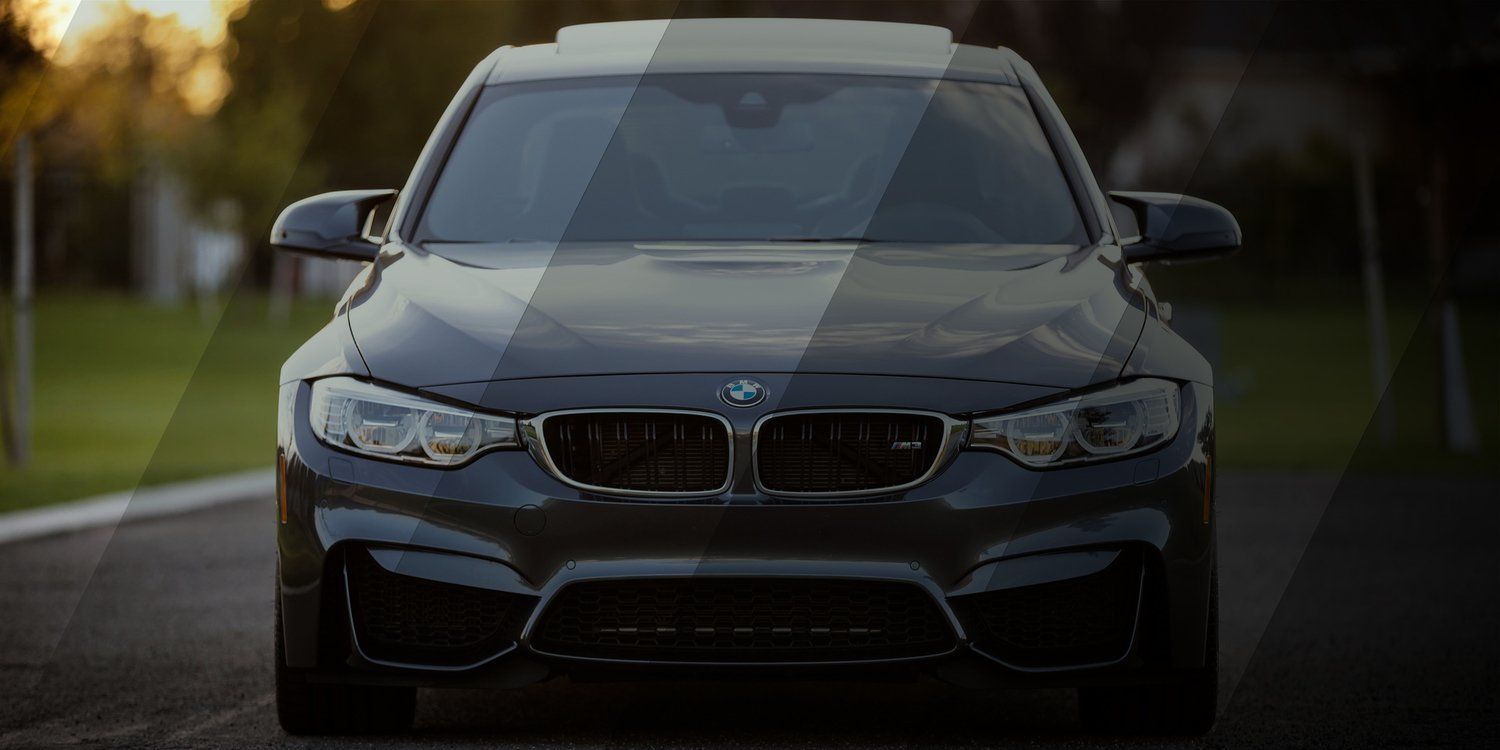 Front view of a black BMW sedan driving on a wet road at dusk