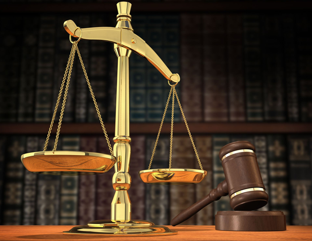 Golden balance scales and a judge’s gavel on a wooden desk, with law books in the background.