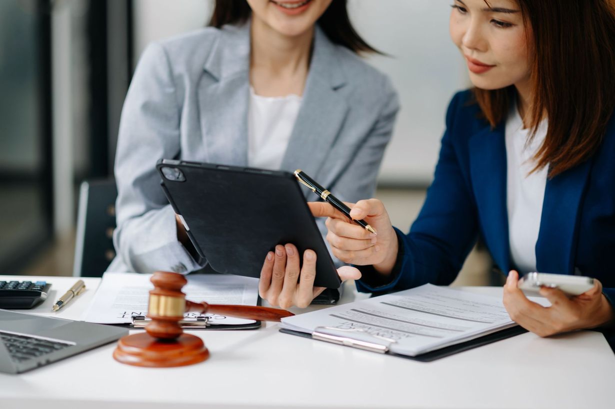 Two coworkers review a tablet and papers at a desk with a gavel and calculator