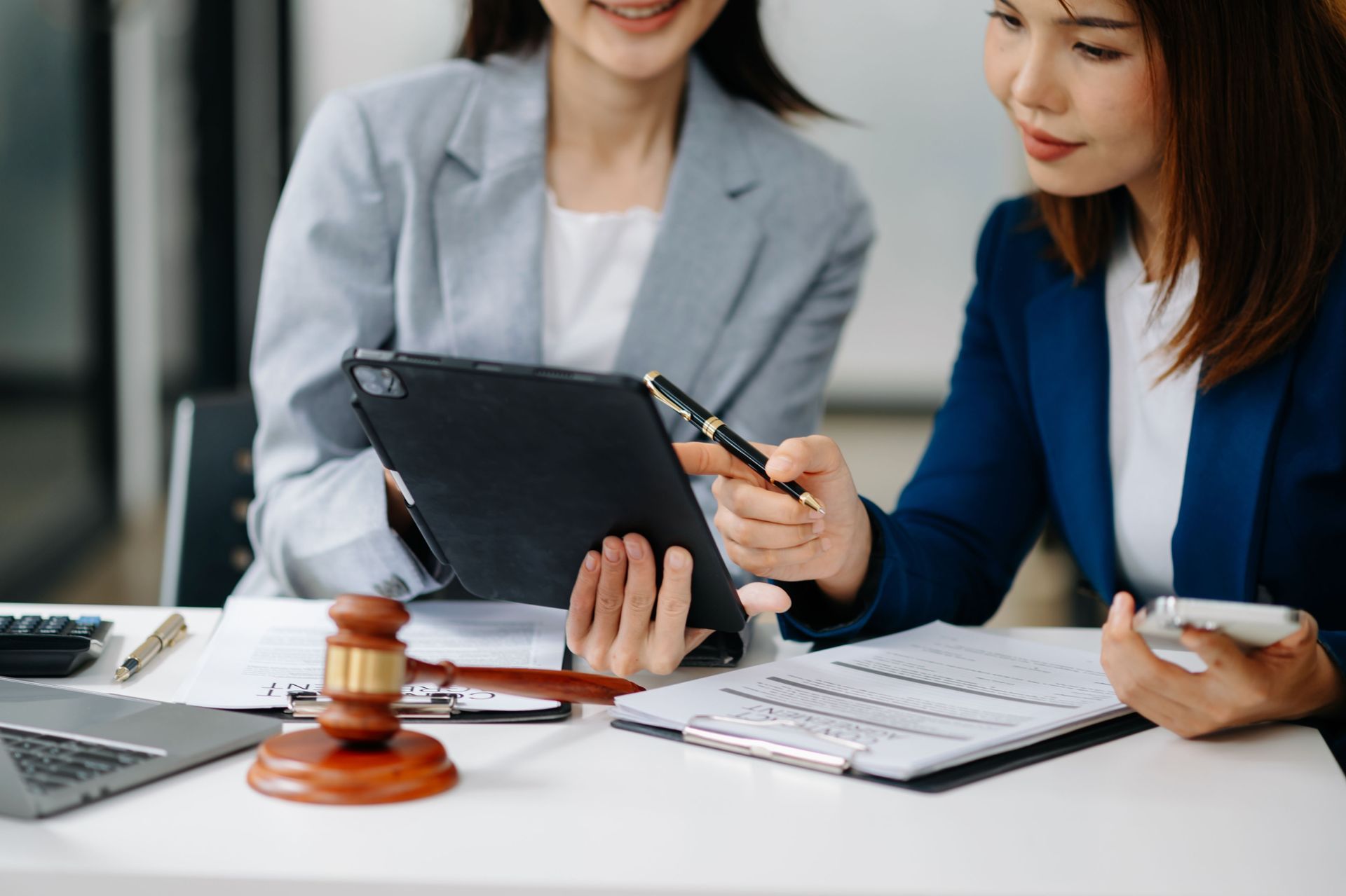 Two coworkers review a tablet and papers at a desk with a gavel and calculator