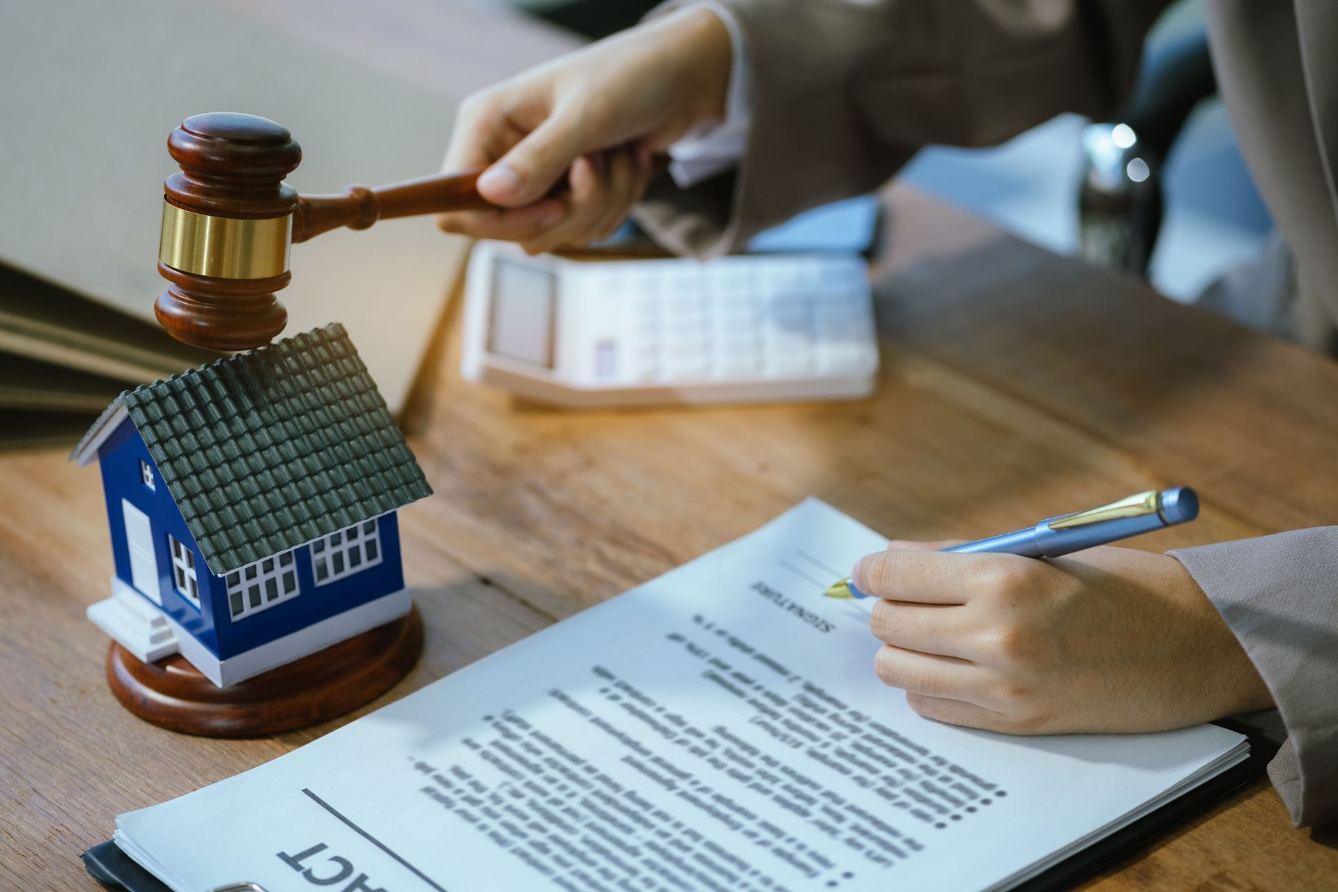 Judge’s gavel over house model as a person signs legal documents at a desk